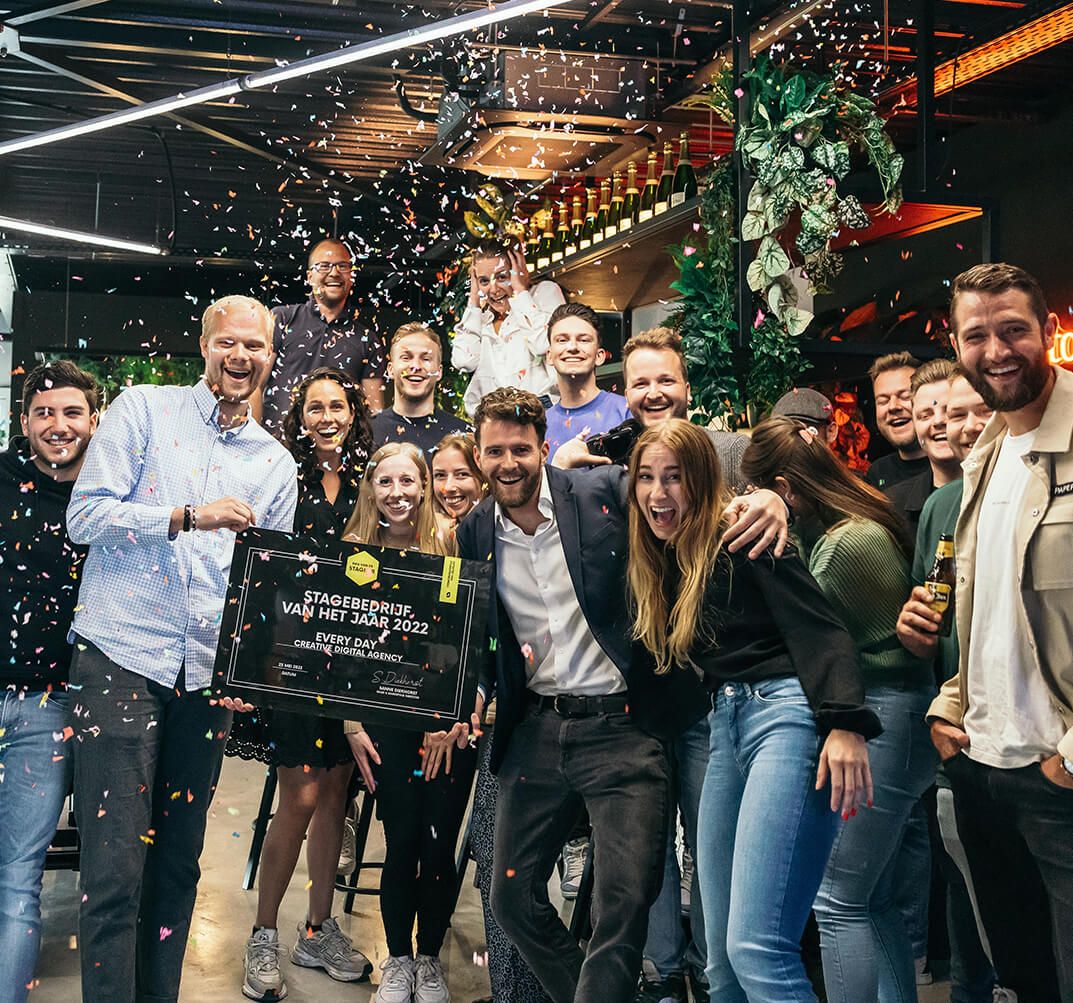 Een vrolijke groep poseert met een plaquette erin, omringd door confetti en brede glimlachen.