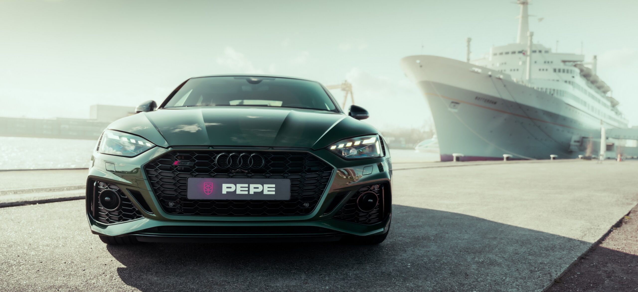 Groene Audi met PEPE-kenteken en Koppert Cress-sticker, geparkeerd naast een groot wit schip aan de kade.
