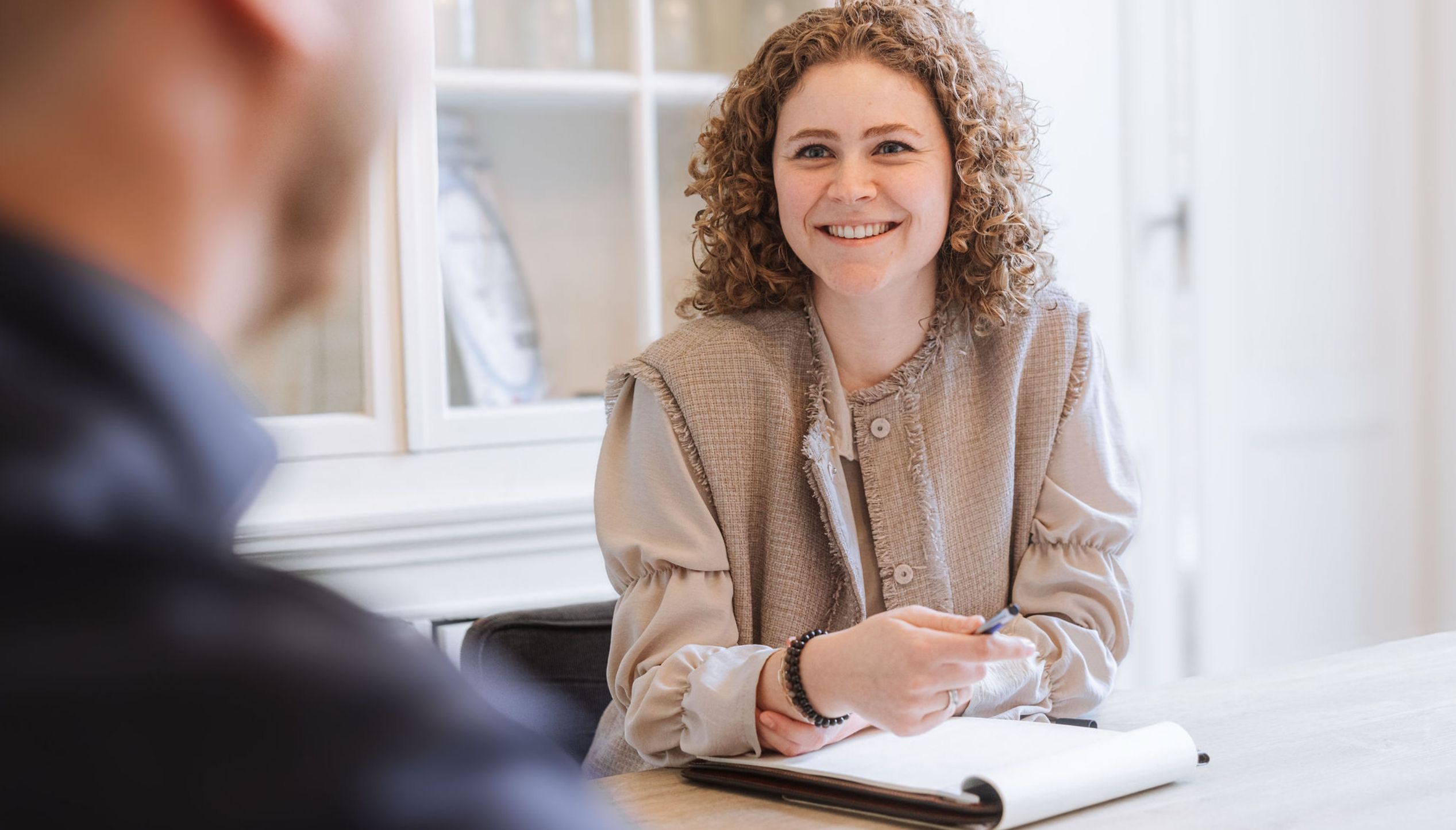 Een lachende vrouw praat met iemand over een notitieboekje tijdens een bijeenkomst van de FIT-groep.