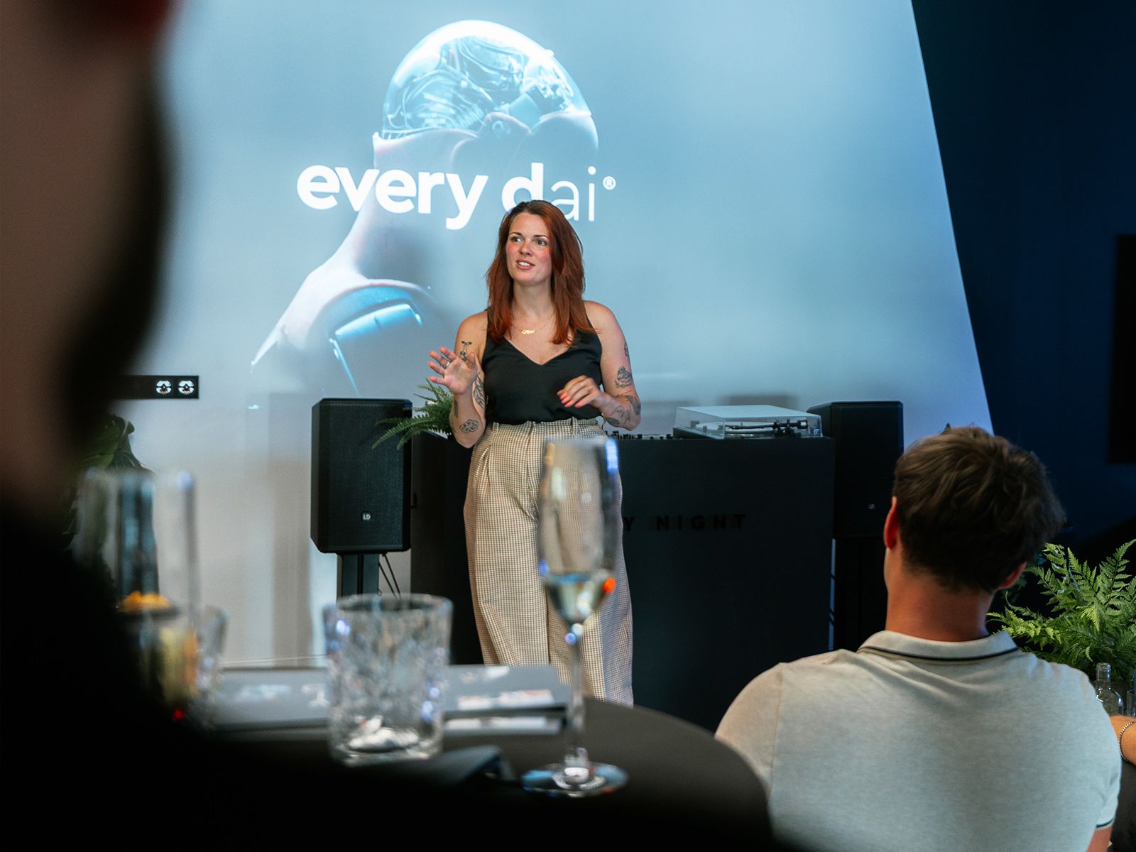Vrouw presenteert aan een publiek voor een scherm dat "every dai" toont met een strak futuristisch ontwerp.