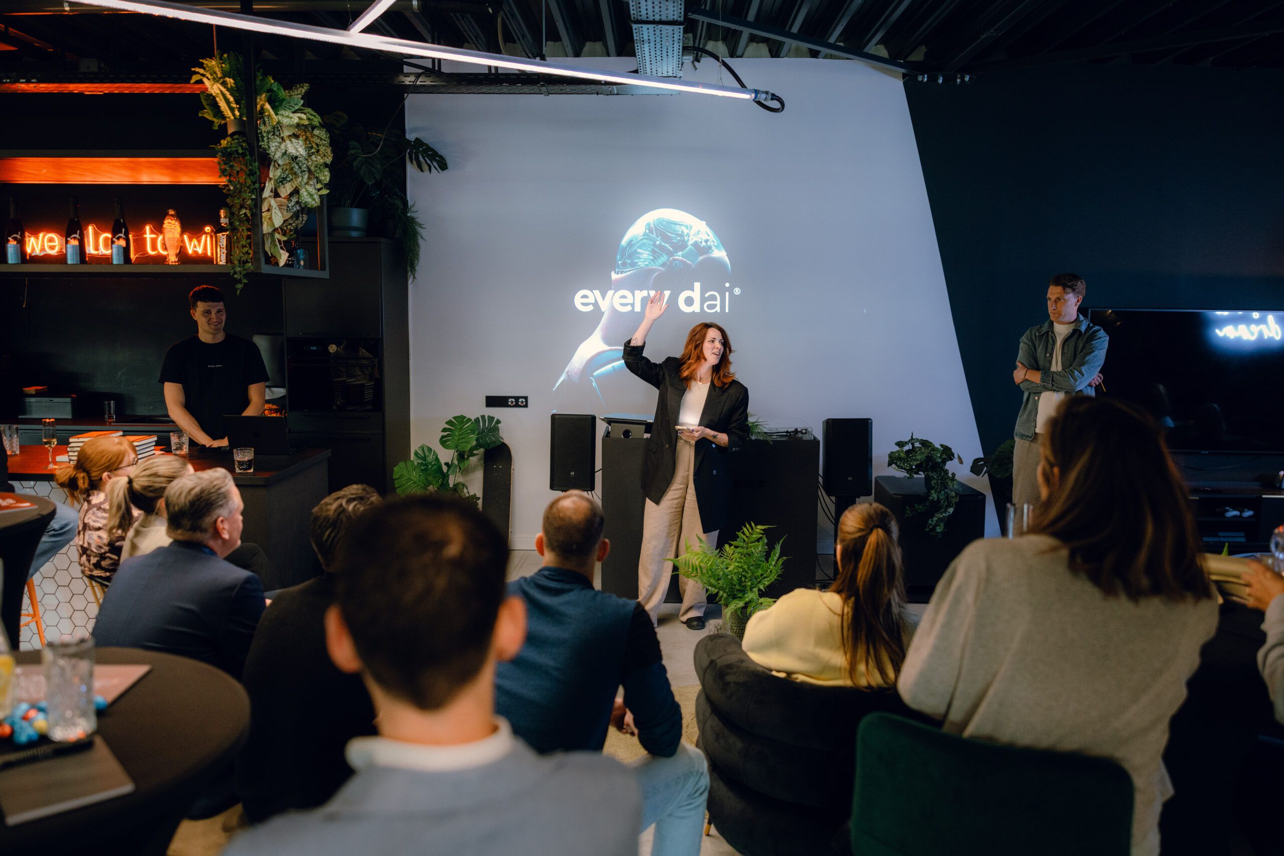 Vrouw presenteert aan een publiek in een strakke kamer, scherm toont "every dai" achter haar.