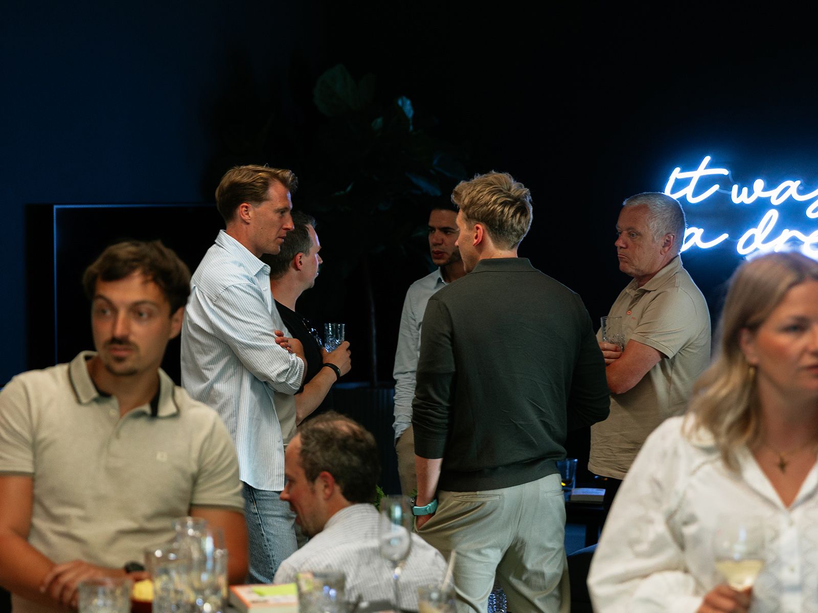 Mensen mengen zich met drankjes in de hand op een schemerig sociaal evenement.