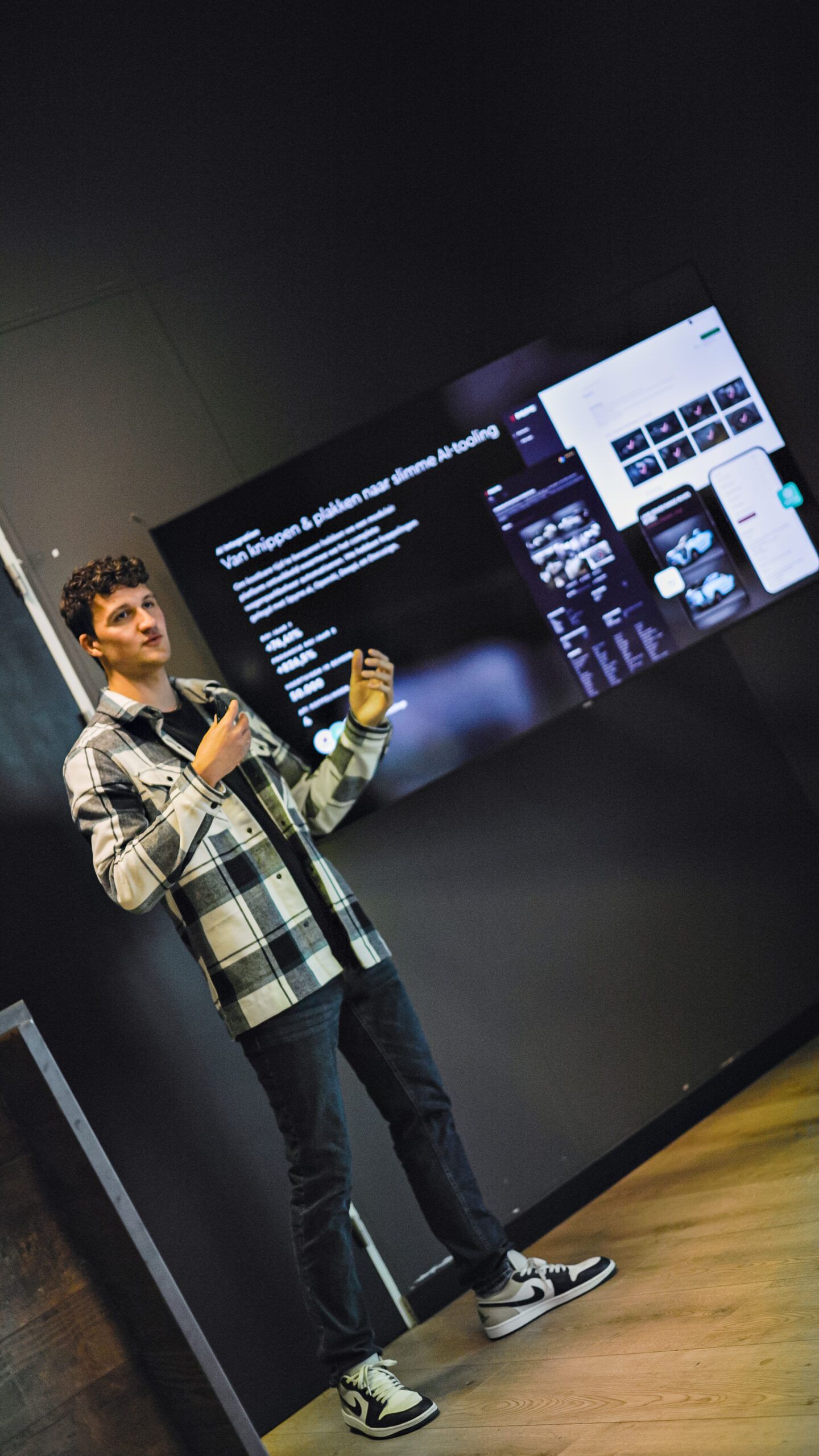 Een spreker met geruite shirts presenteert dia's op een groot scherm in een strakke, moderne ruimte.