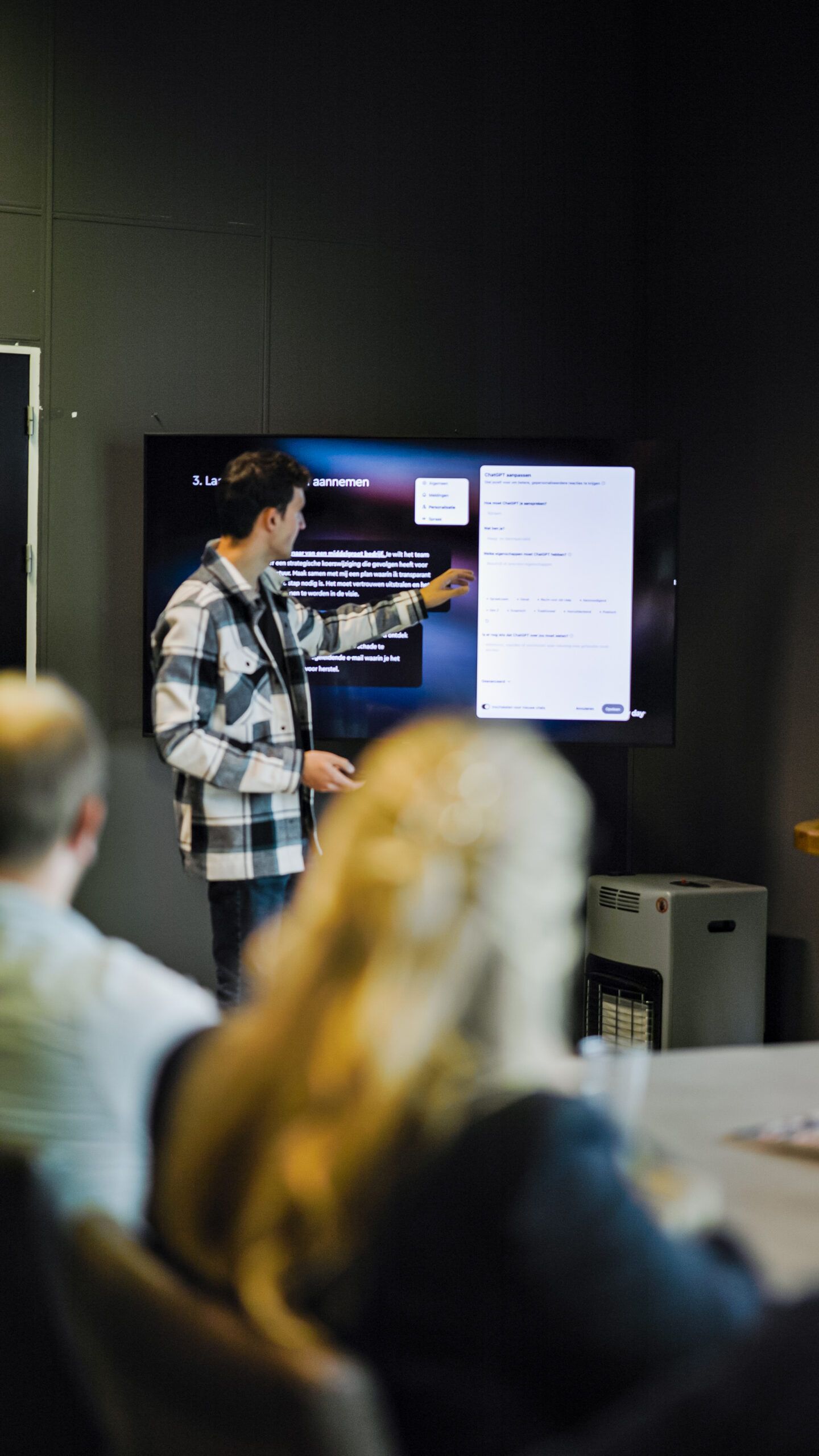 Presentator wijst naar dia's op een scherm terwijl hij het publiek toespreekt in een vergaderzaal.
