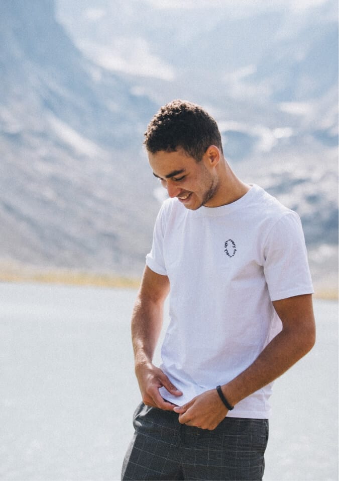 Lachende man in wit T-shirt met wazige bergen en een meer op de achtergrond.