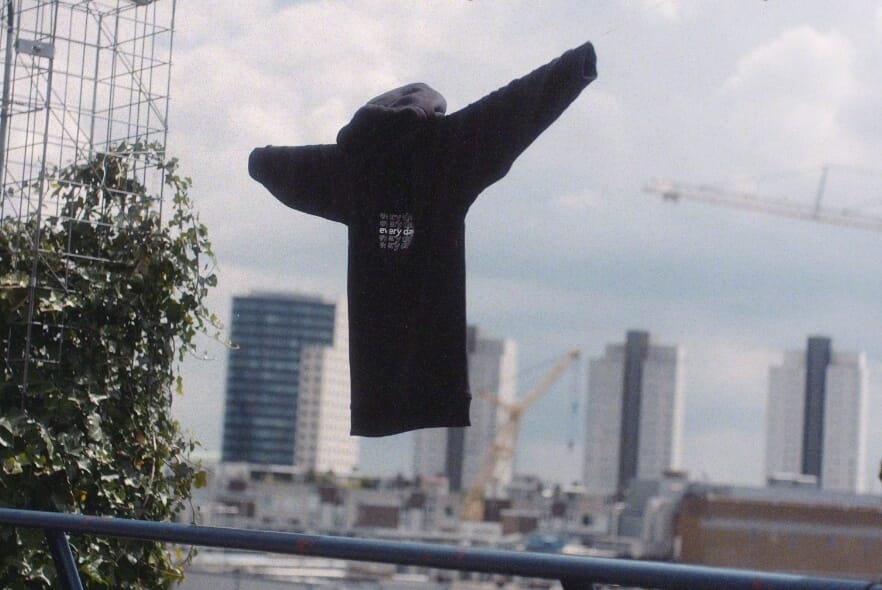 Hoodie die zweeft boven de skyline van een stad, omlijst door gebouwen en kranen.