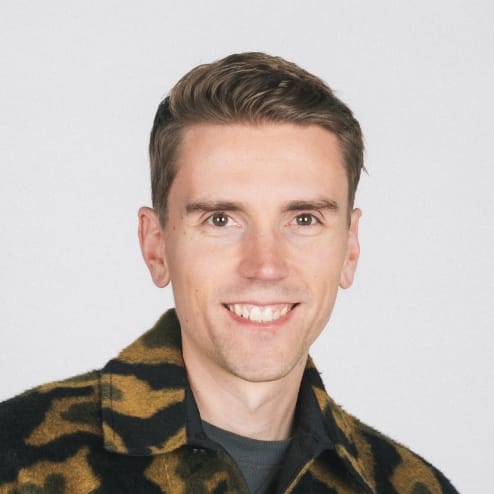 Grijnzend in camouflagekleding tegen een minimalistische achtergrond.