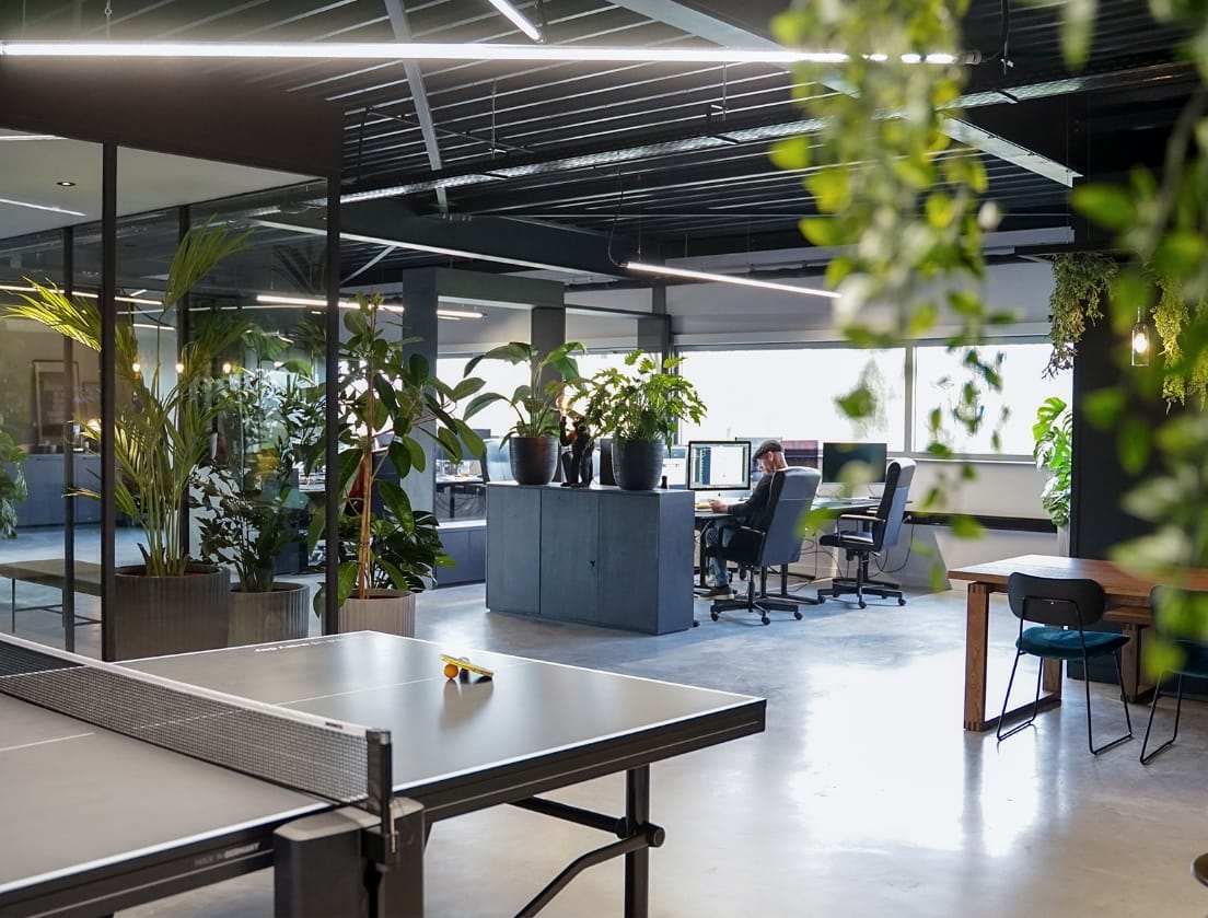 Trendy kantoor: planten, een pingpongtafel en geconcentreerde mensen die op de achtergrond aan een bureau werken.