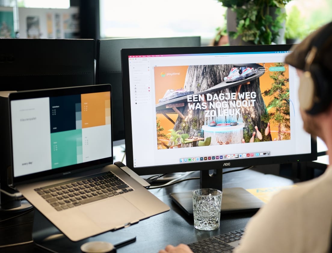 Een gebruiker werkt aan digitale ontwerpen met behulp van zowel een laptop als twee monitoren aan zijn bureau.