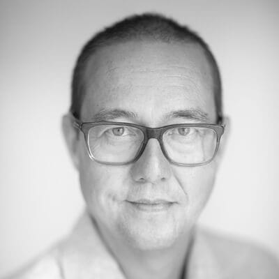 Zwart-witfoto: man met bril, kort haar, licht shirt.