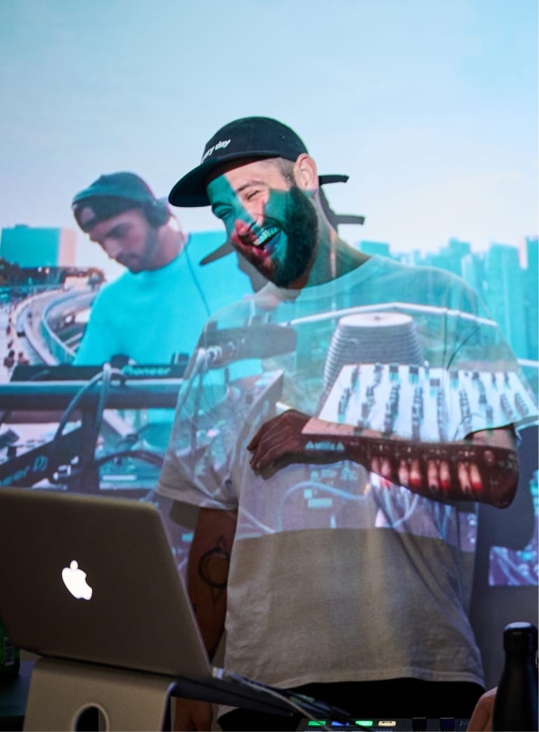 DJ draait nummers op een laptop, stadsgezicht en mengpaneel verlichten zijn vibe.