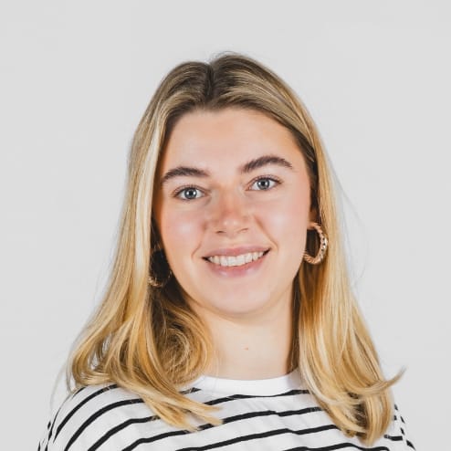 Blonde jongeman met hoepels en een gestreept shirt, lachend tegen een effen achtergrond.