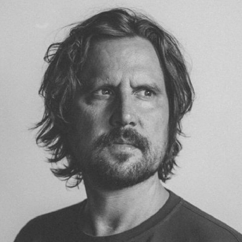 Zwart-witportret: man met schouderlang haar, een baard, die opzij kijkt.