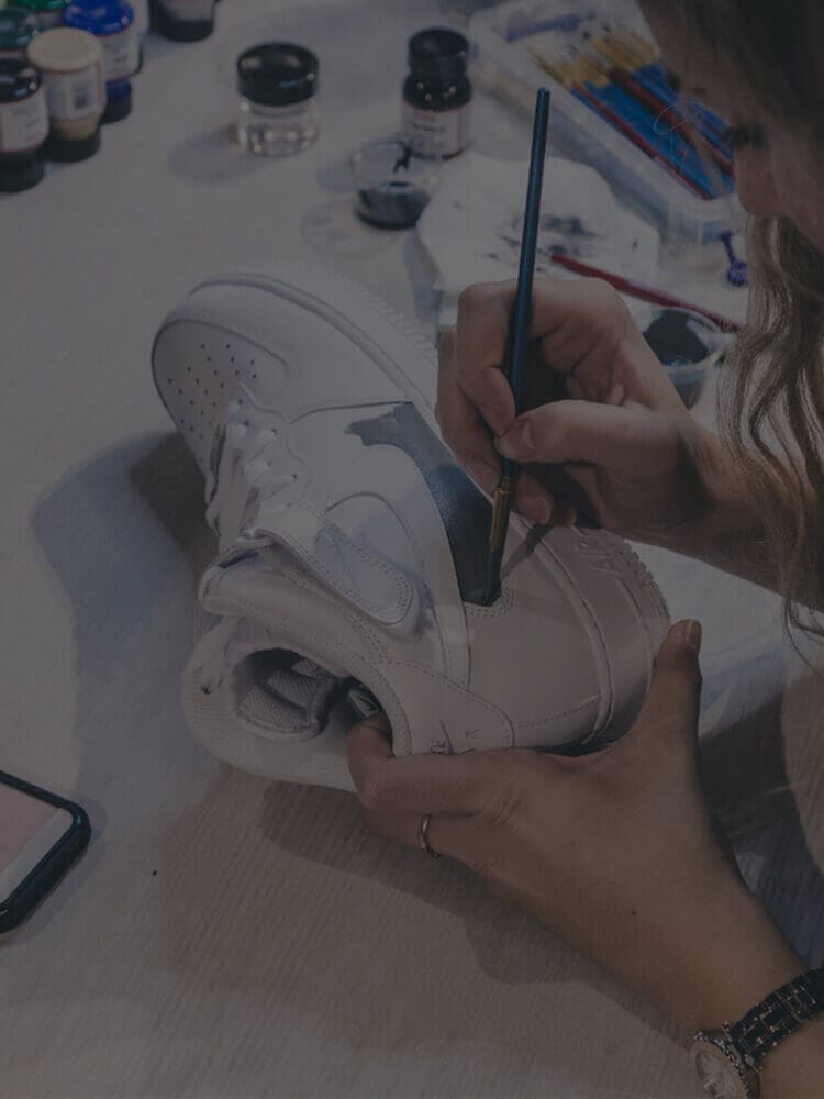 Iemand knapt een witte sneaker op met een kwast en creëert zo een uniek exemplaar voor de exclusieve Customs by BB-lijn.