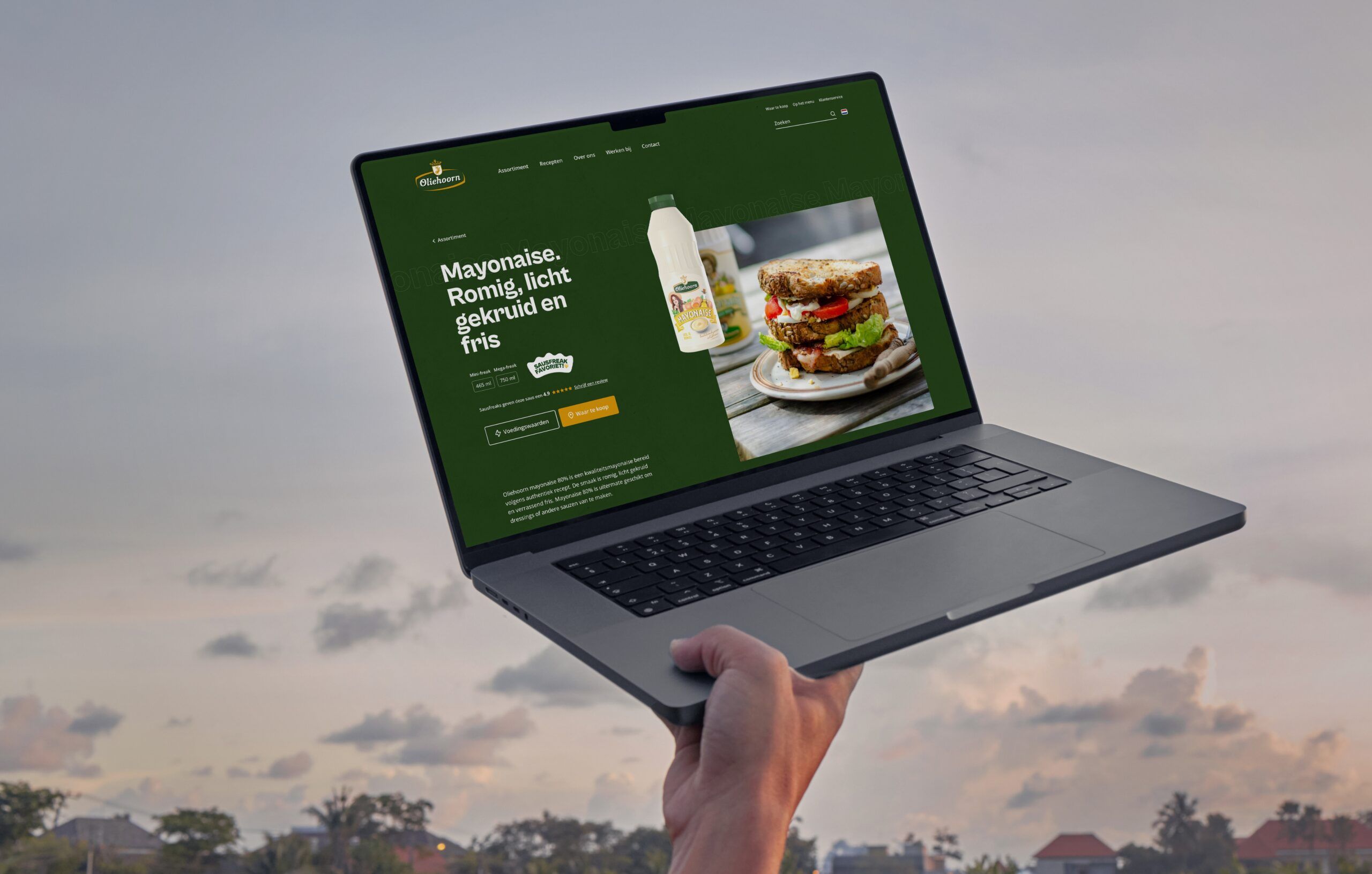 Een laptop met daarop een eetcafé met een hamburger en saus, tegen een bewolkte lucht.