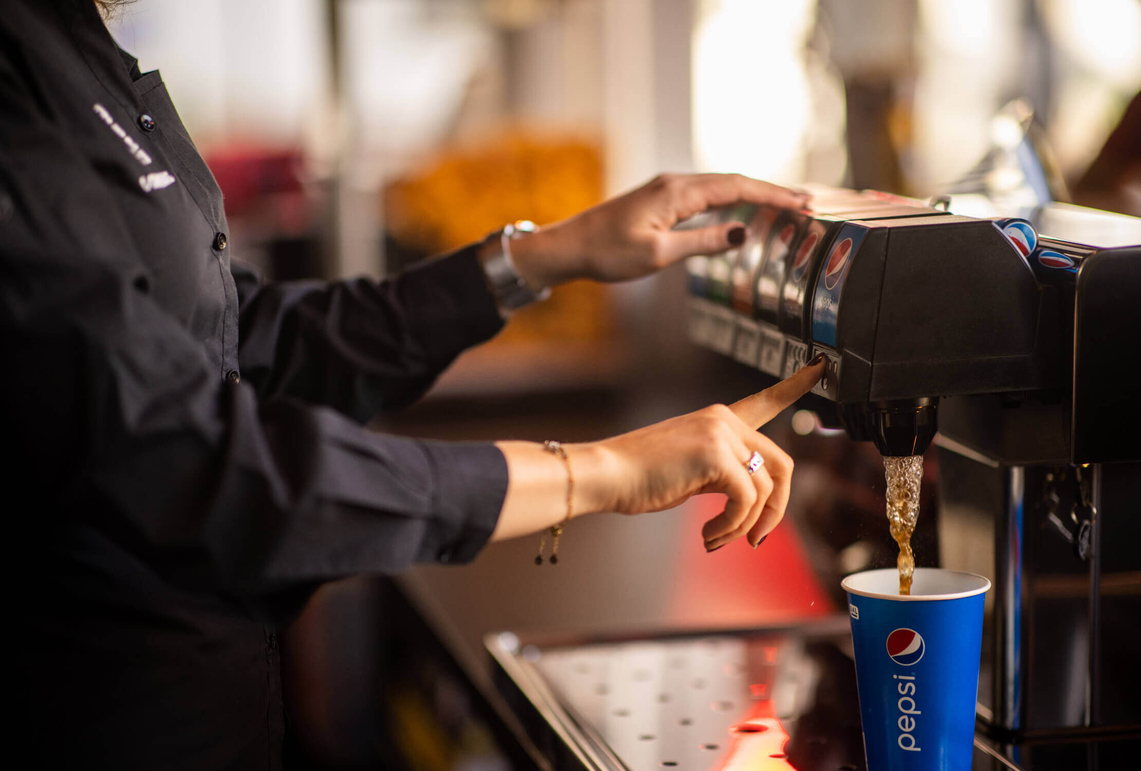 Een werknemer in uniform vult een beker met Pepsi uit de frisdrankautomaat.