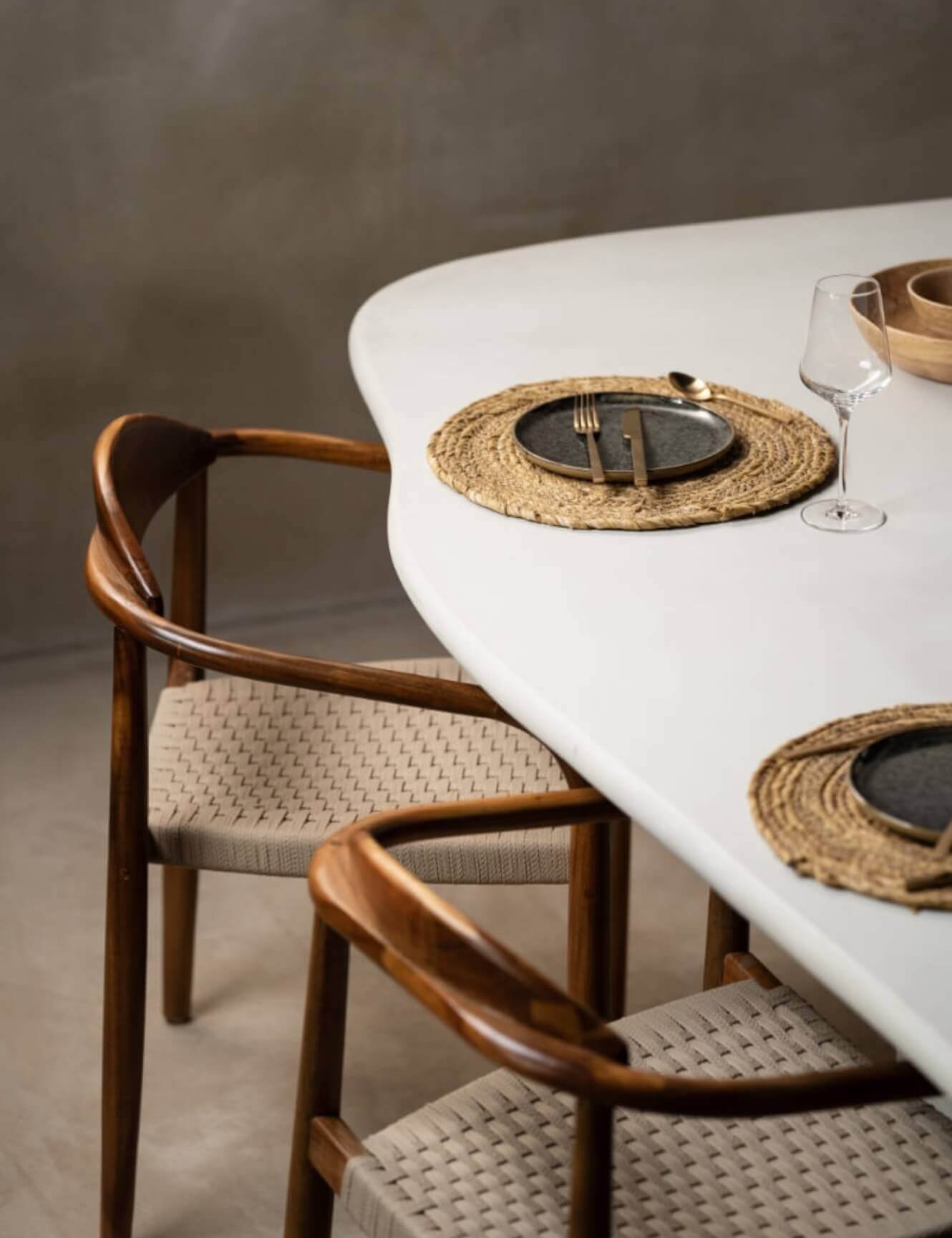 Strak dineren: witte tafel, houten stoelen, geweven matten, zwarte borden, bestek en wijnglas.