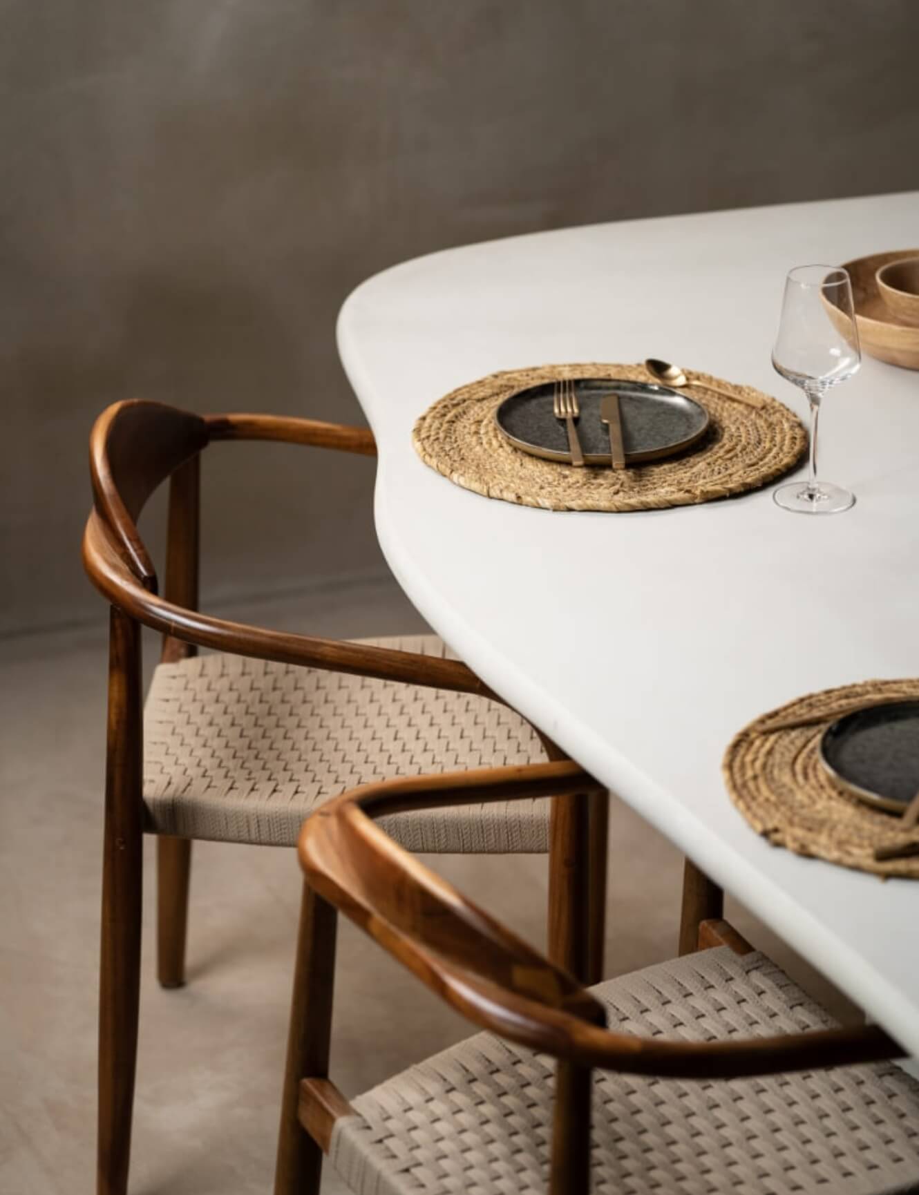 Minimalistische eethoek: geweven placemats, borden, bestek, wijnglazen, houten stoelen.