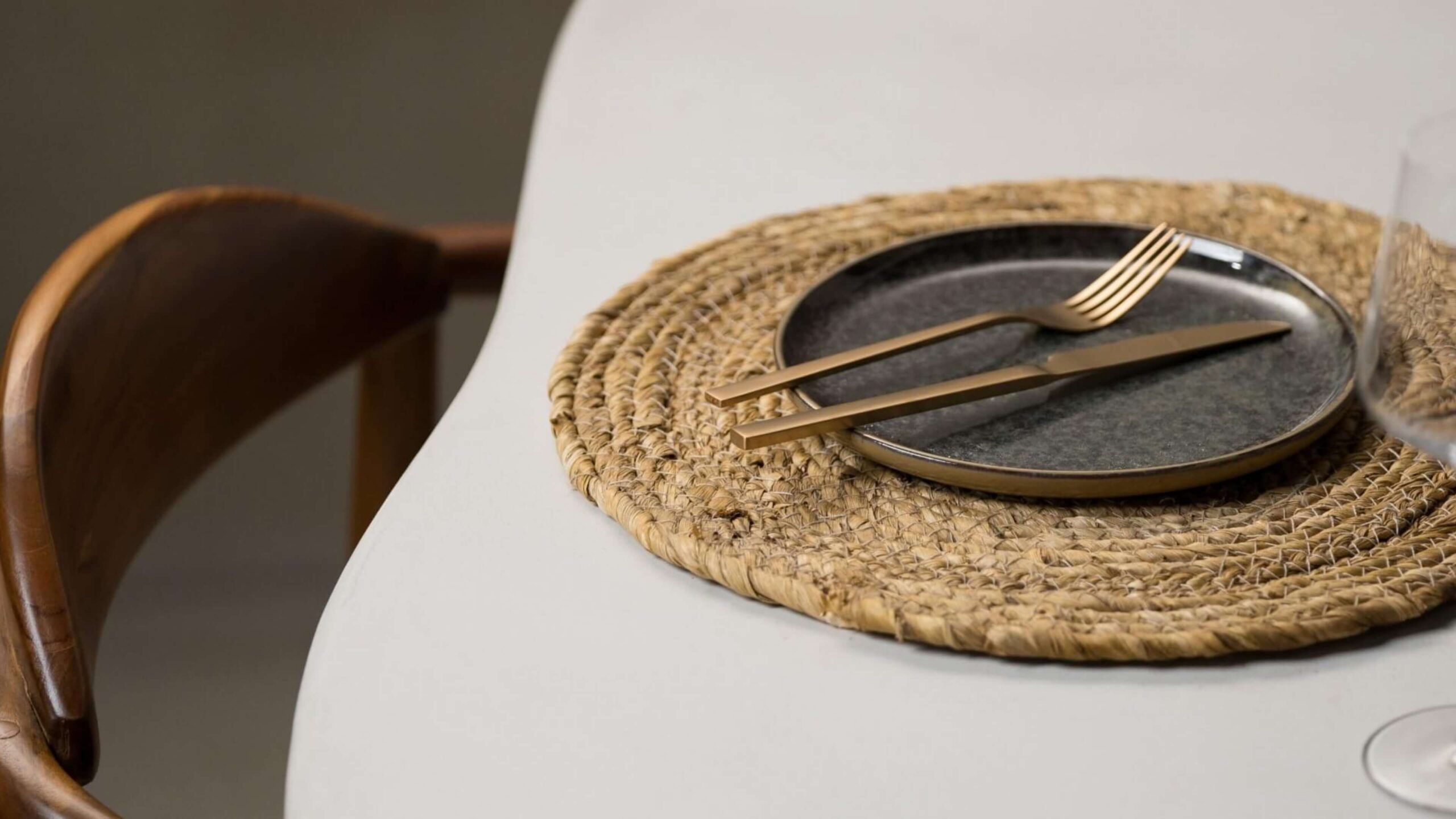 Zwart bord, gouden bestek op geweven placemat; strakke, moderne tafelopstelling.