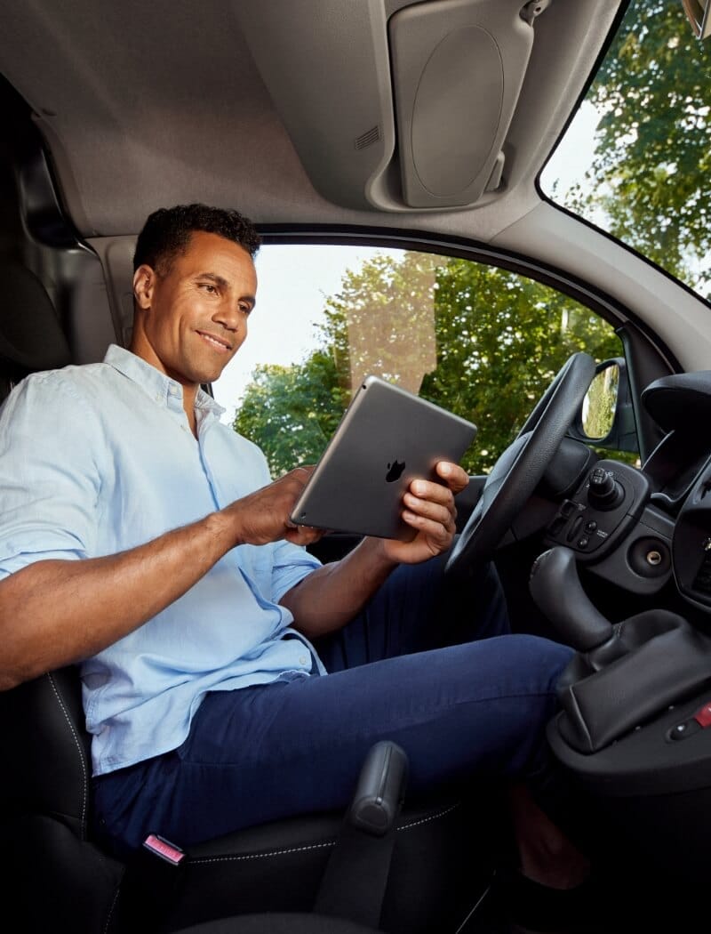 Chauffeur in een lichtblauw shirt gebruikt een tablet terwijl hij in de auto zit.