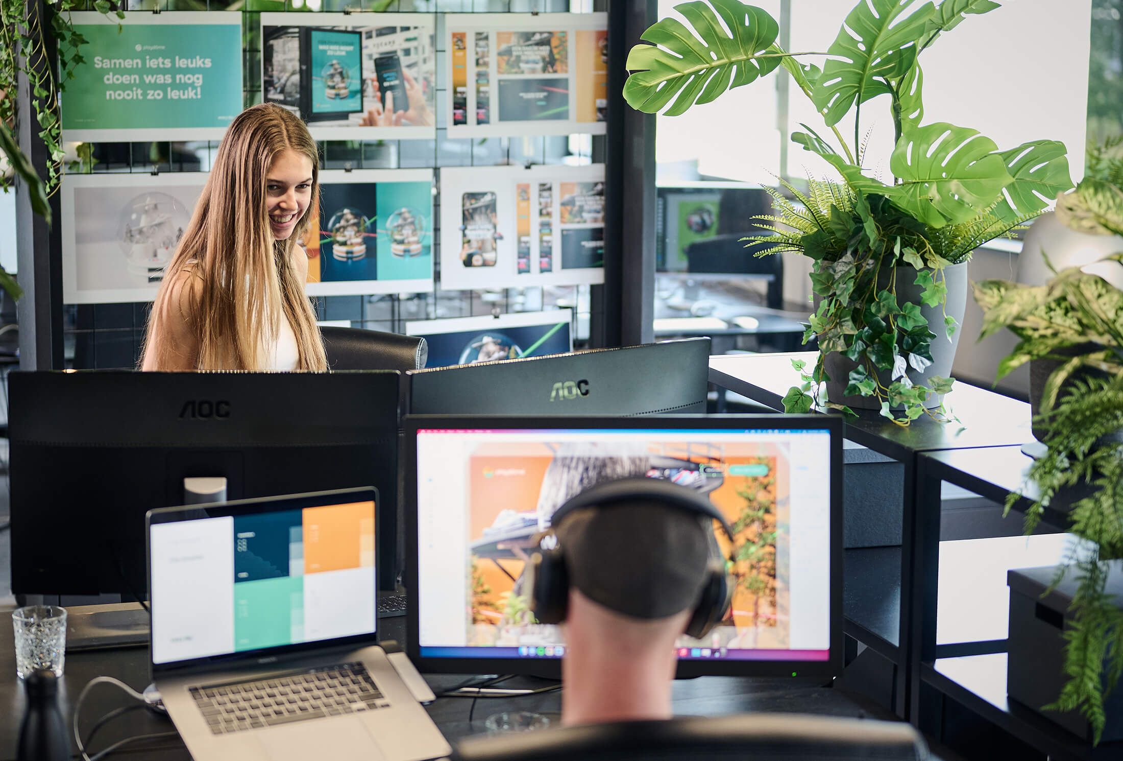 In een levendige, groene ruimte werken een man en een vrouw geconcentreerd aan hun computers in de creatieve omgeving van Playdome.