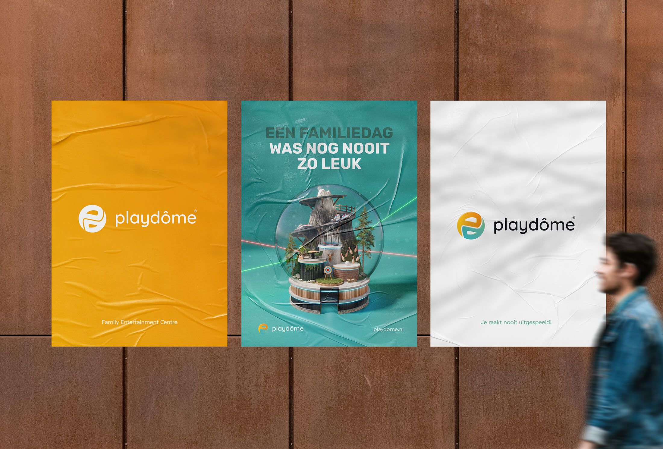 Een man loopt langs drie posters op een muur, waarvan er twee het logo van Playdôme dragen.