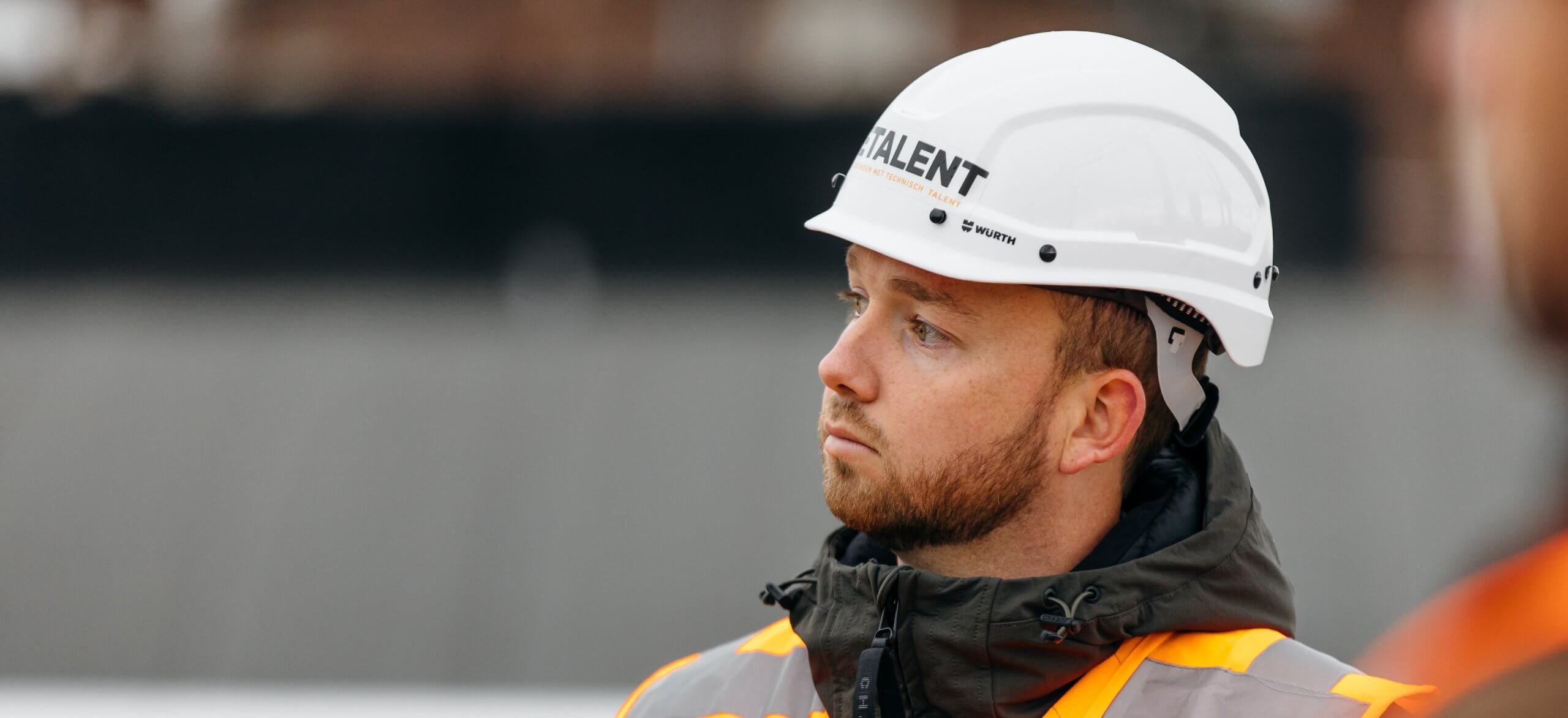 Bouwvakker met witte helm en oranje vest kijkt aandachtig opzij.