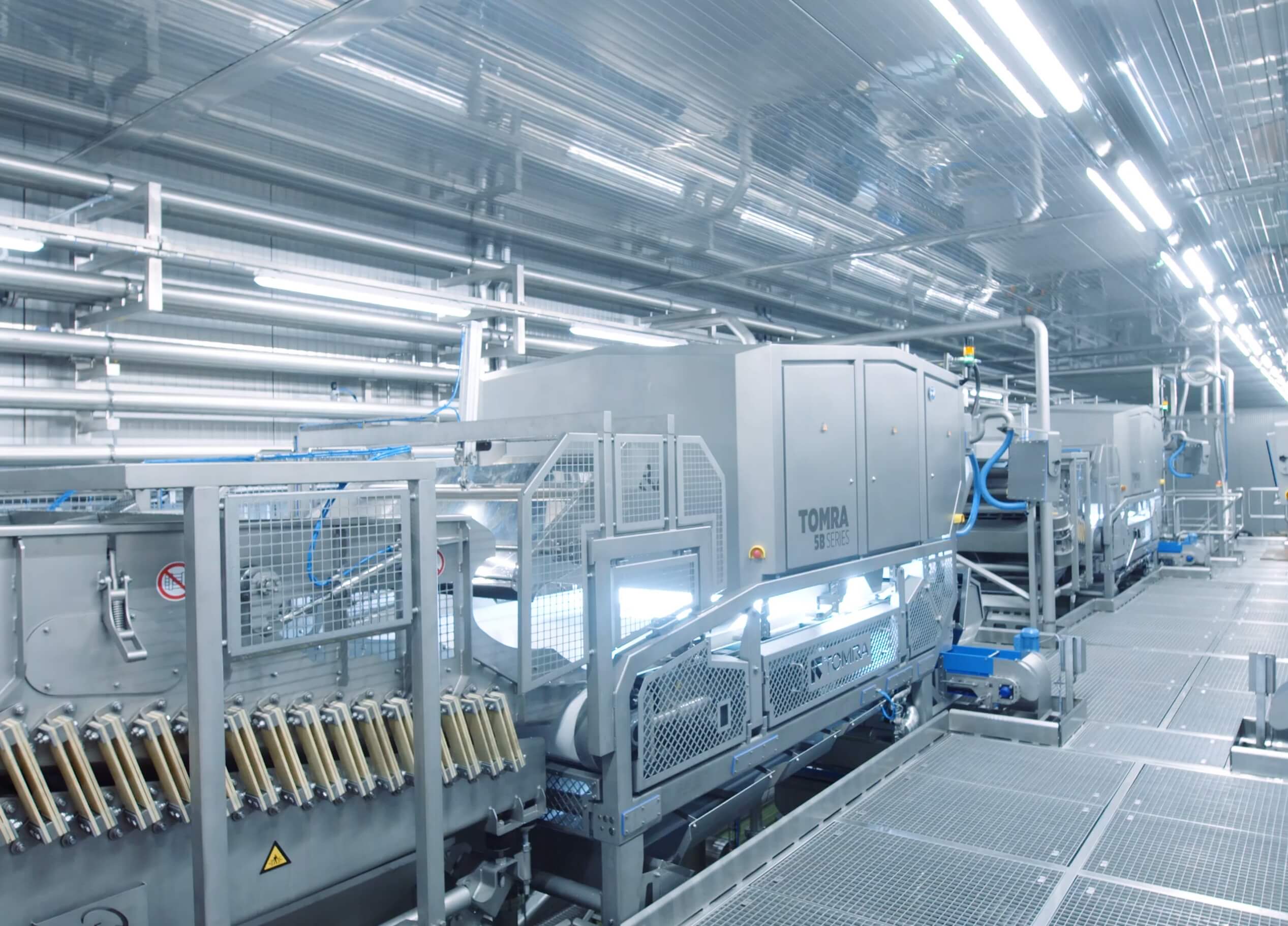 Moderne fabriek: ingewikkelde machines, metalen buizen en tandwielen verlicht door felle plafondlampen.