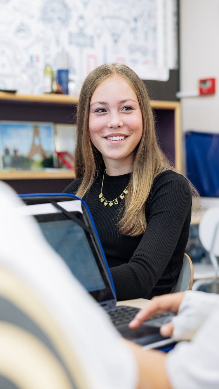 Langharige student lacht terwijl hij in de klas een laptop gebruikt.