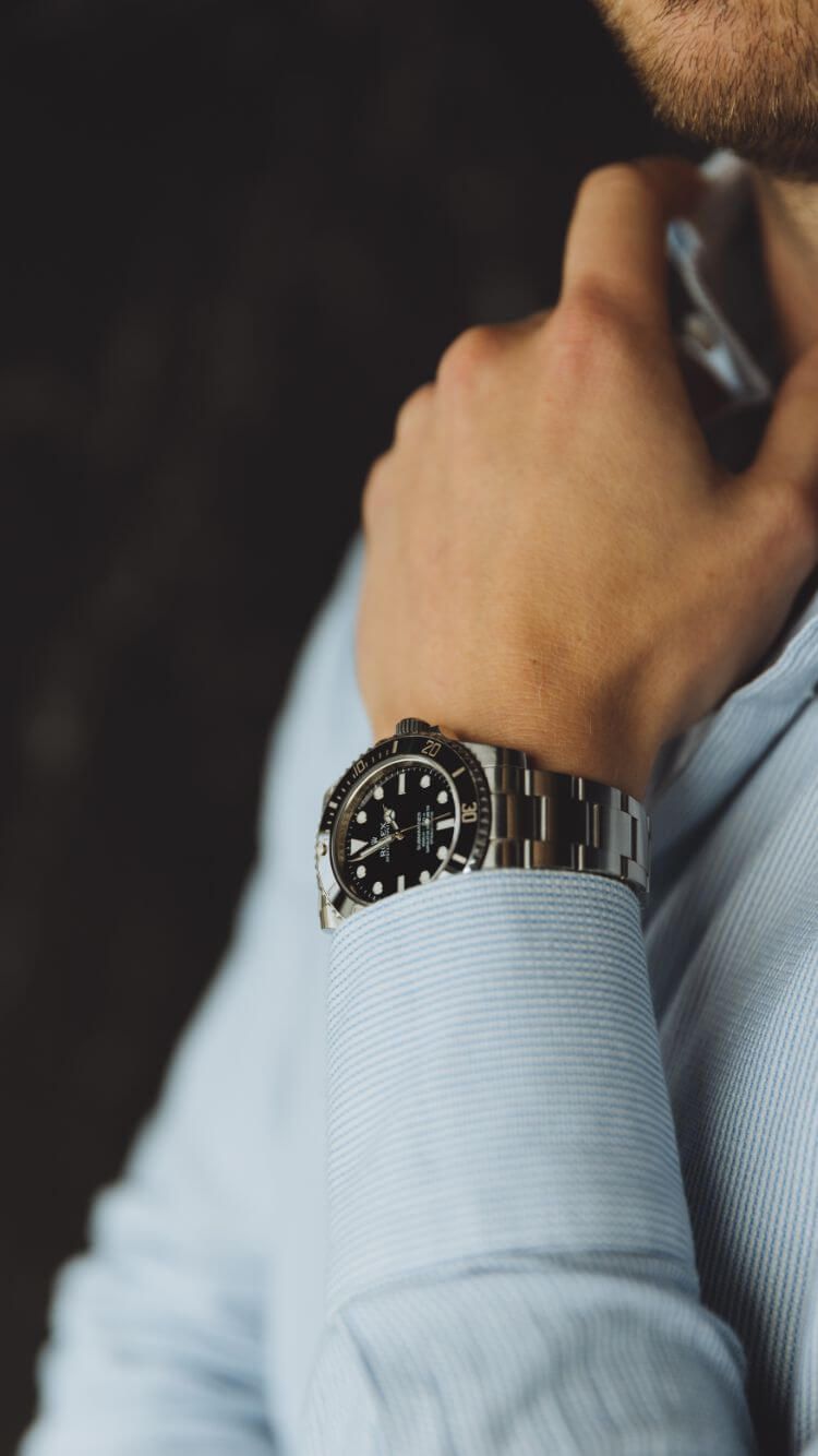 Iemand zet de kraag van een overhemd recht en draagt een zilveren horloge met een zwarte wijzerplaat.