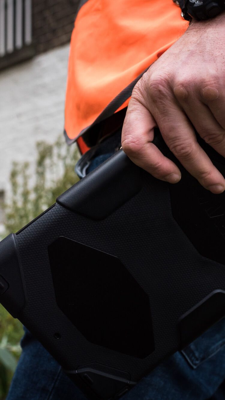 Een persoon in een oranje vest toont zijn TB-vaardigheden met een robuuste zwarte tablet buiten.