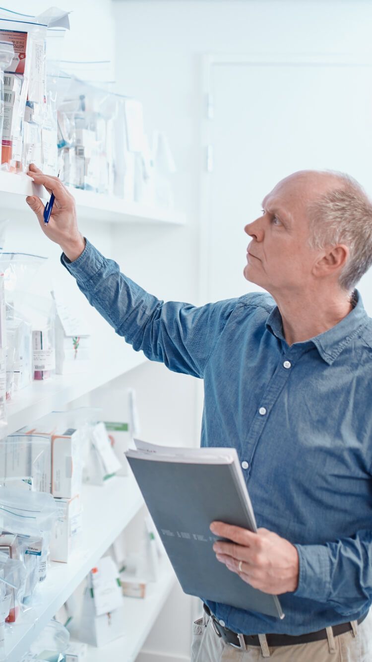 Een man in een blauw shirt houdt een notitieboekje en een pen vast en scant de planken vol producten in doorzichtige zakken.