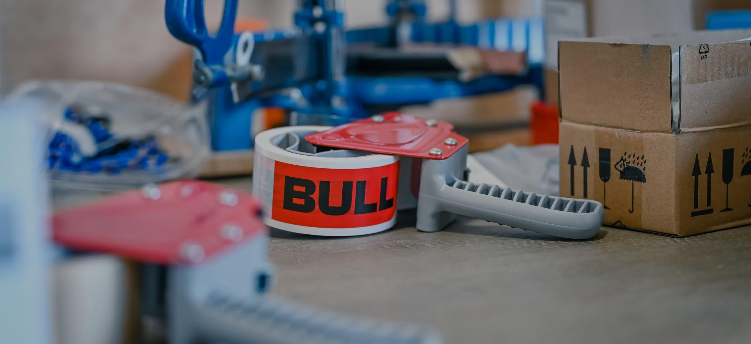 Op tafel staan plakbandhouders en een kartonnen doos, klaar voor gebruik.