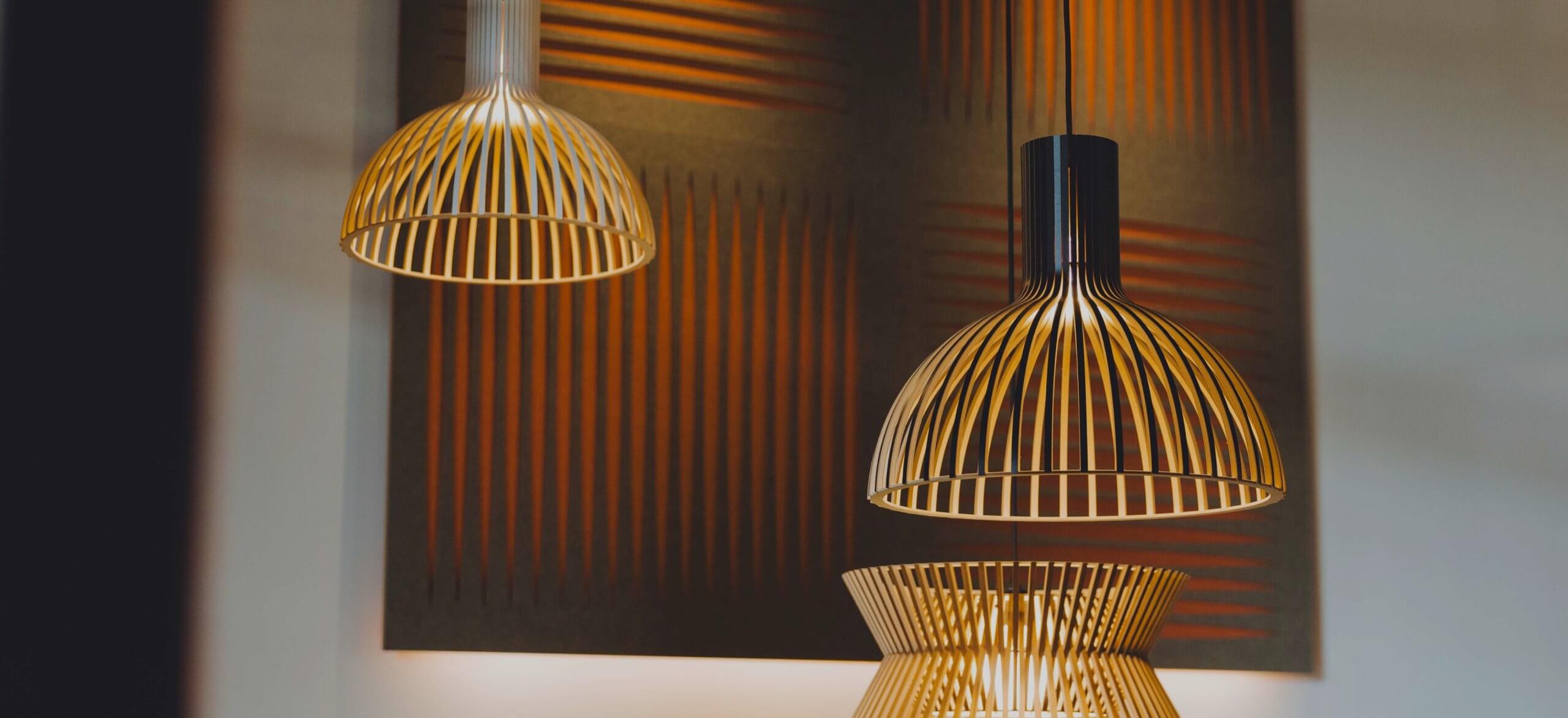 De moderne hanglampen van TunnelmaDesign met geribbelde gouden kappen springen in het oog op een wandpaneel met structuur.