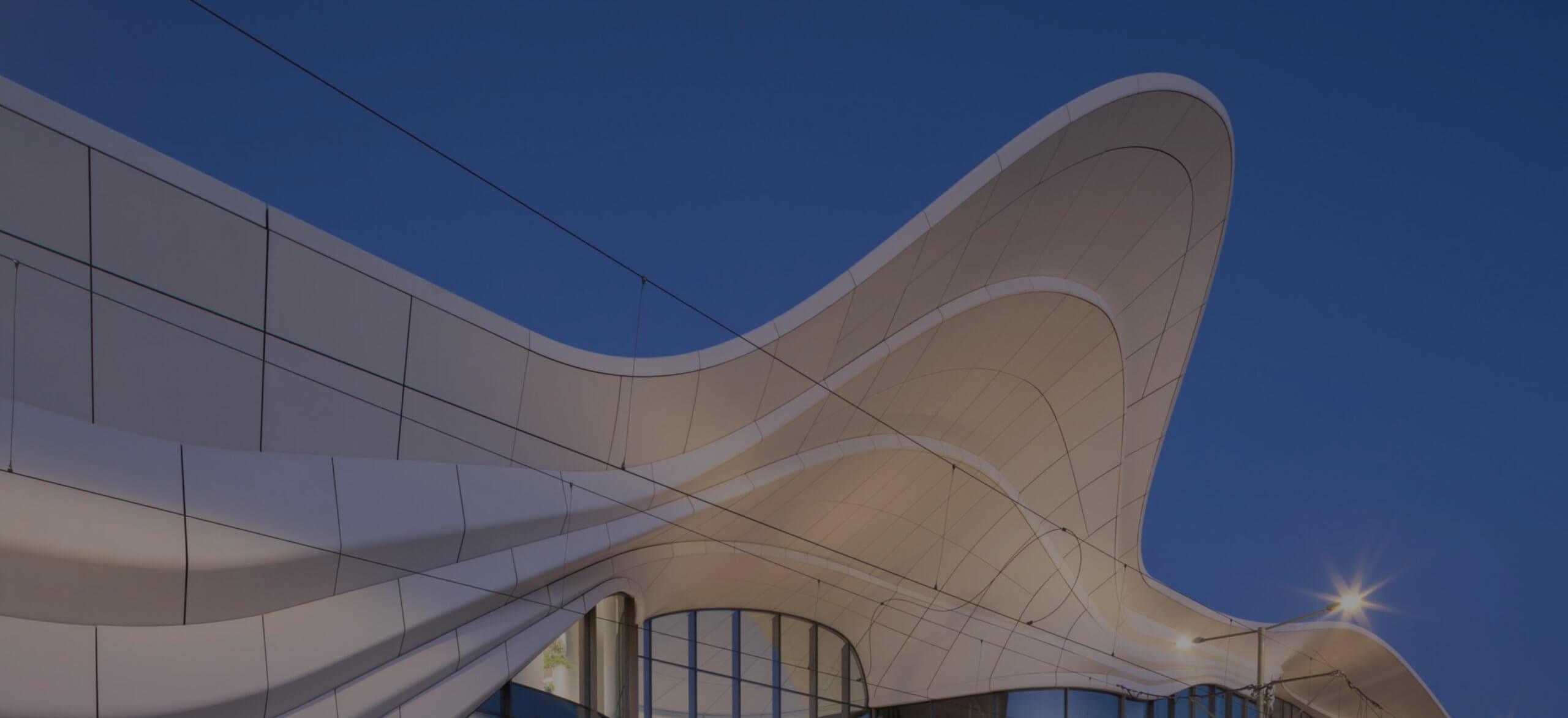 Een gebogen, golvend dak siert een futuristisch gebouw onder een heldere avondhemel.