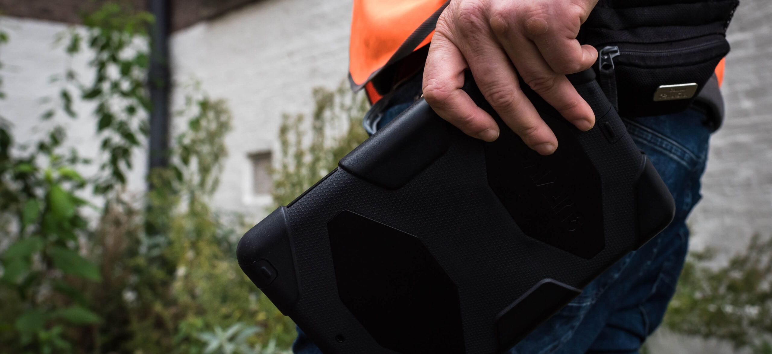 Een TB-expert in een oranje vest houdt buiten een robuuste tablet vast.