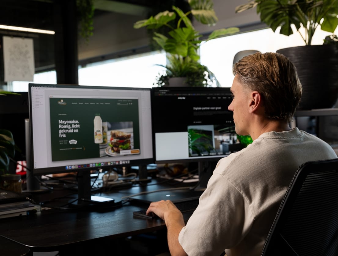 Iemand werkt op twee beeldschermen in een strak kantoor vol planten.