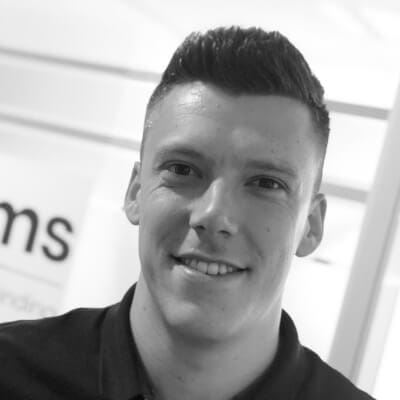 Grijswaardenfoto: Lachende persoon met kort donker haar in een zwart shirt, onscherpe achtergrond.