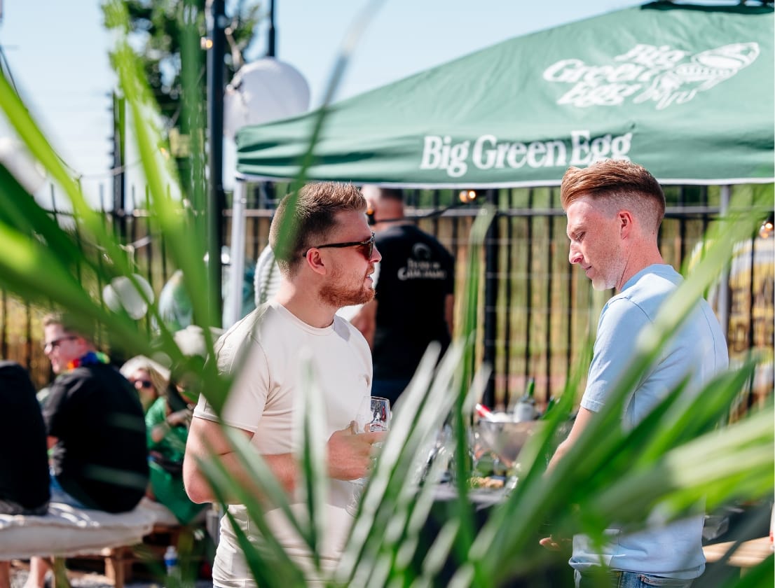 Twee mannen praten buiten een groene tent, met op de voorgrond planten om hen heen.