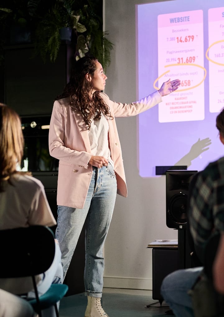 In een donkere kamer presenteert iemand in vrijetijdskleding gegevens op een projectiescherm.