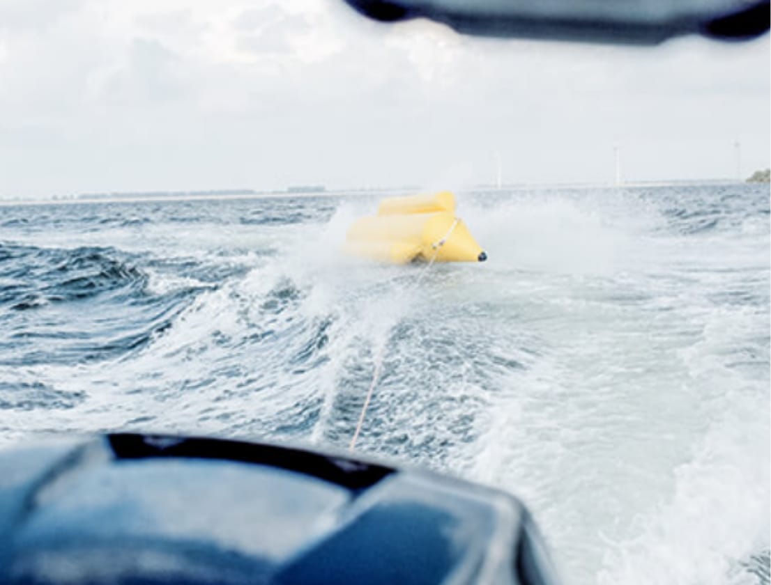 Een gele opblaasbare band raast over de woelige golven van de oceaan, voortgetrokken door een speedboot.