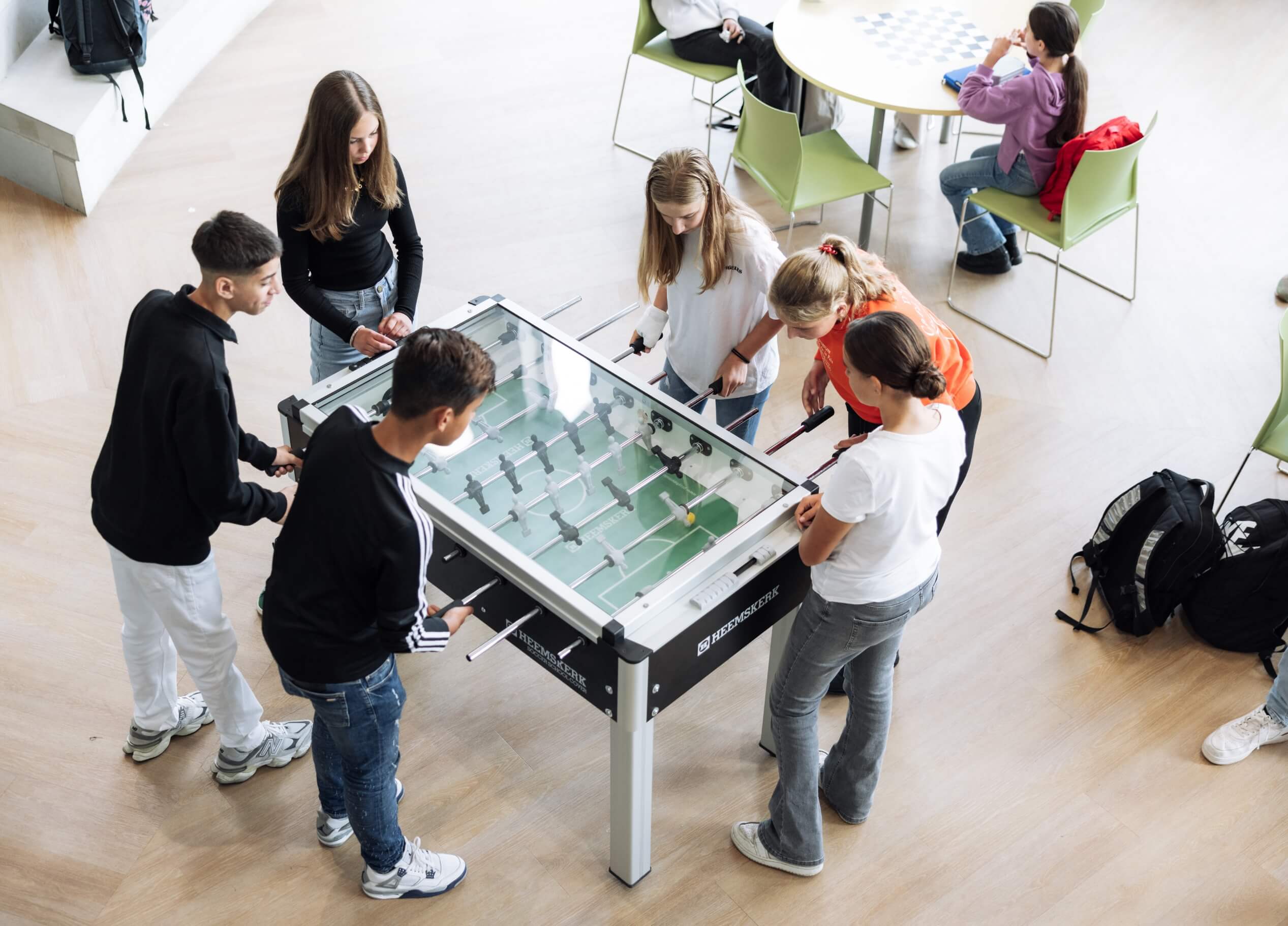 Jongeren spelen tafelvoetbal in een lichte kamer, anderen ontspannen zich aan een tafeltje ernaast.