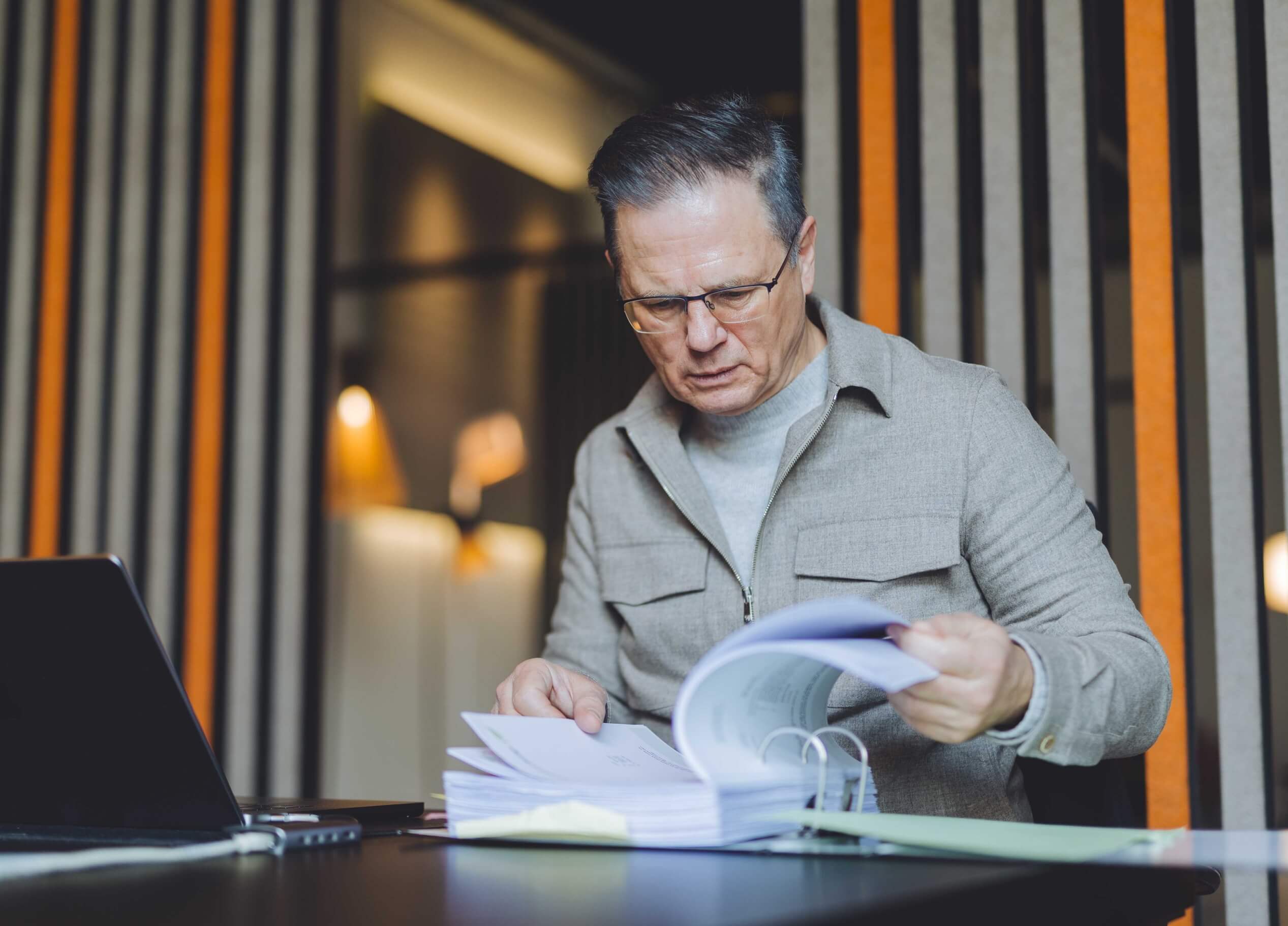 In een strak kantoor van TunnelmaDesign bekijkt een man met een bril documenten, met zijn laptop naast zich.