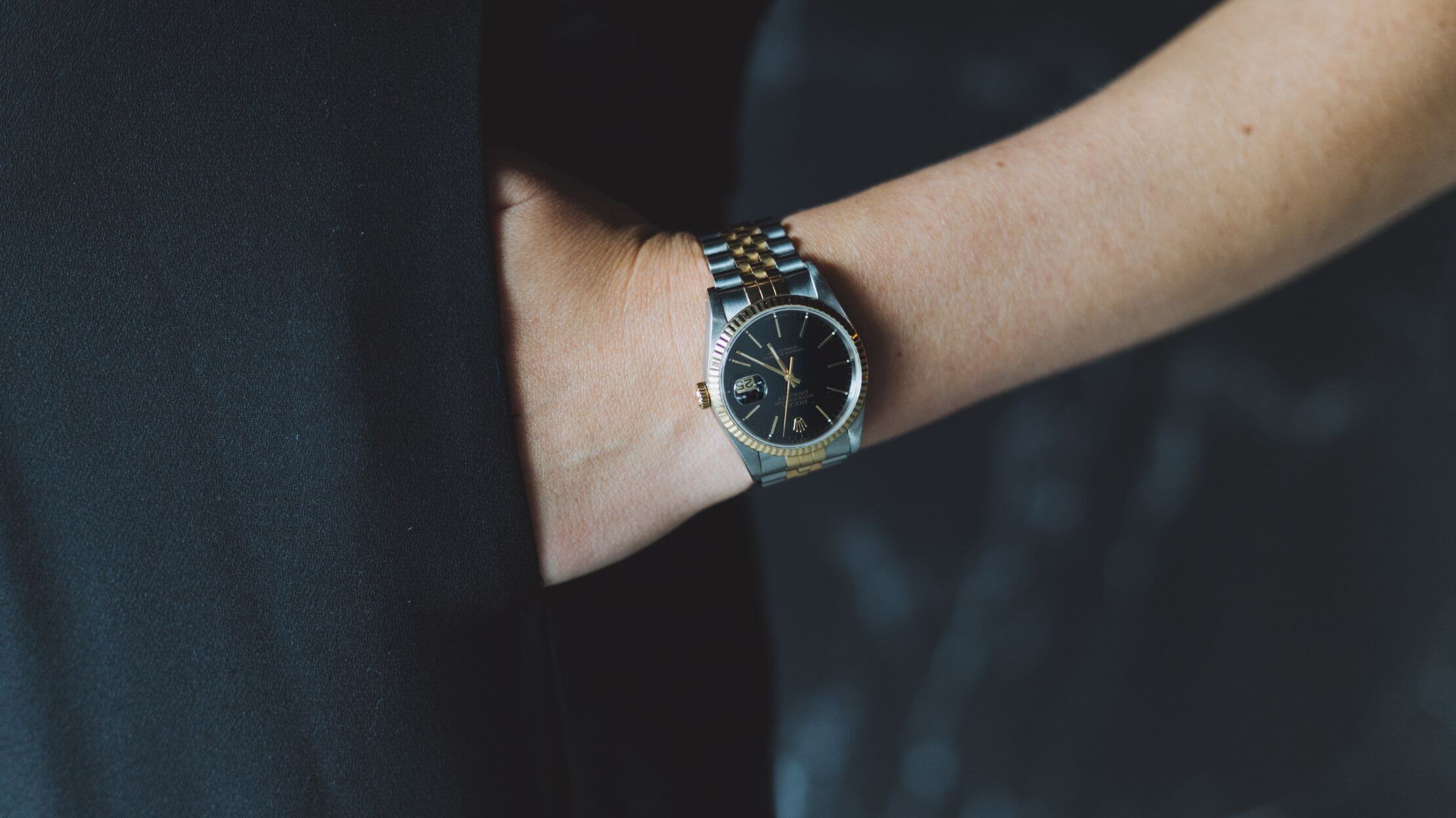 Hand in zak, zwart en zilver horloge tegen een donkere achtergrond.