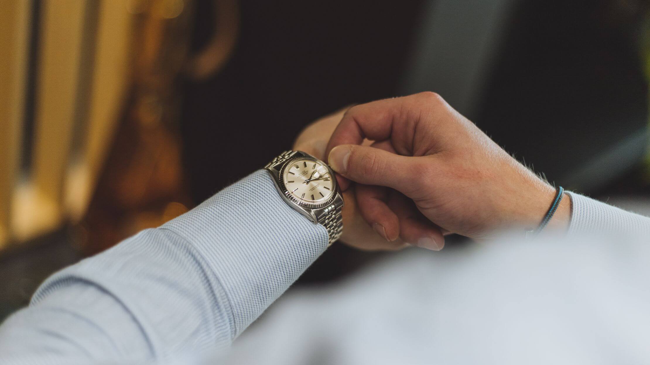 Iemand kijkt op zijn zilveren metalen horloge om te zien hoe laat het is.