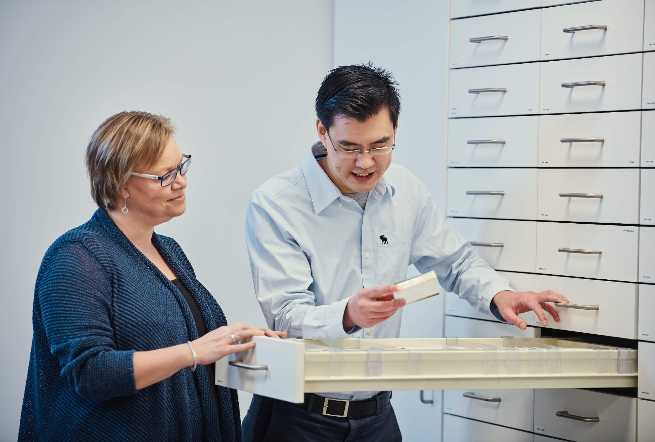 Twee mensen controleren een lade in een kantoor met witte kasten.