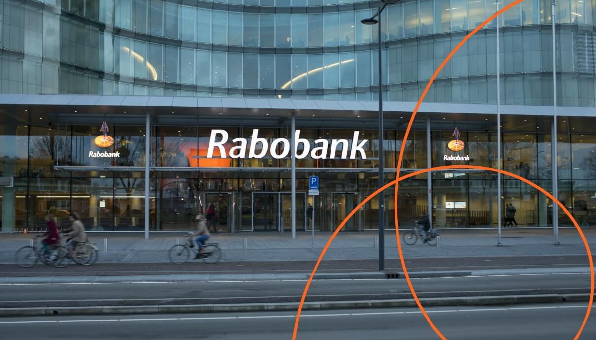 Fietsers passeren een strak Rabobankgebouw, versierd met oranje rondingen.