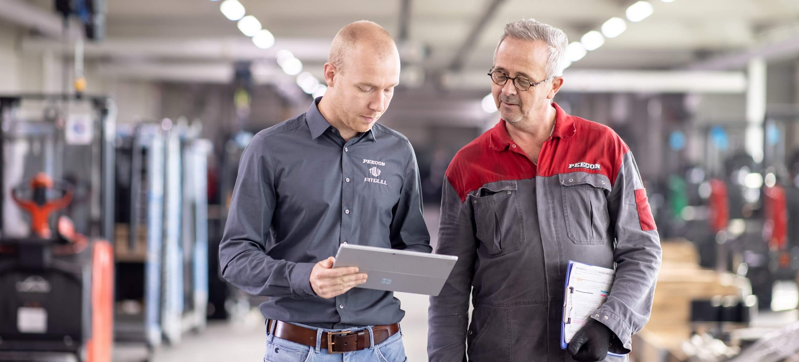 Twee arbeiders in uniform bekijken een tabletscherm in het magazijn.