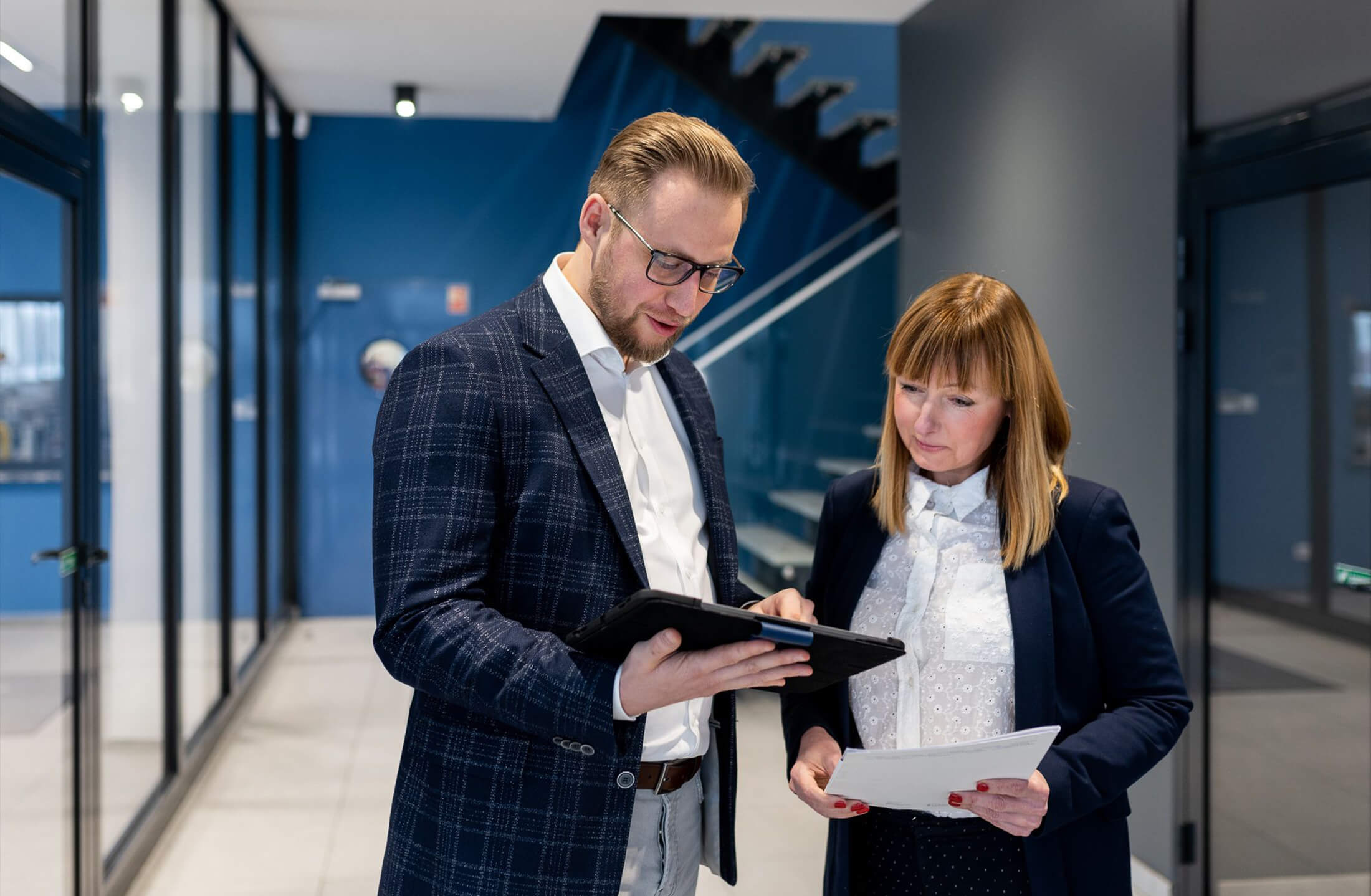Een man en een vrouw bespreken documenten in de strakke hal van het kantoor van Viscon Group.