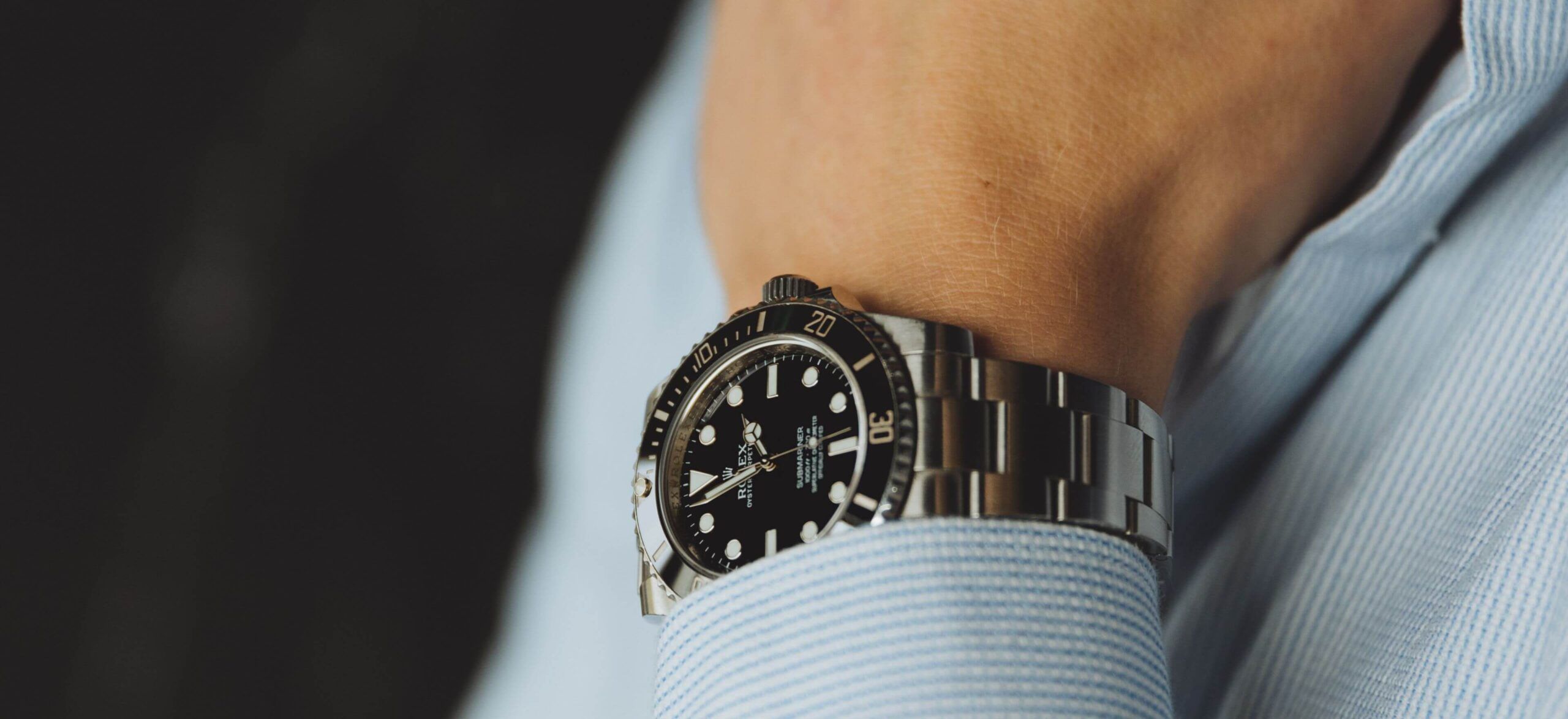 Close-up: Horloge van roestvrij staal, zwarte wijzerplaat, draaibare lunette, om de pols met een blauw shirt.
